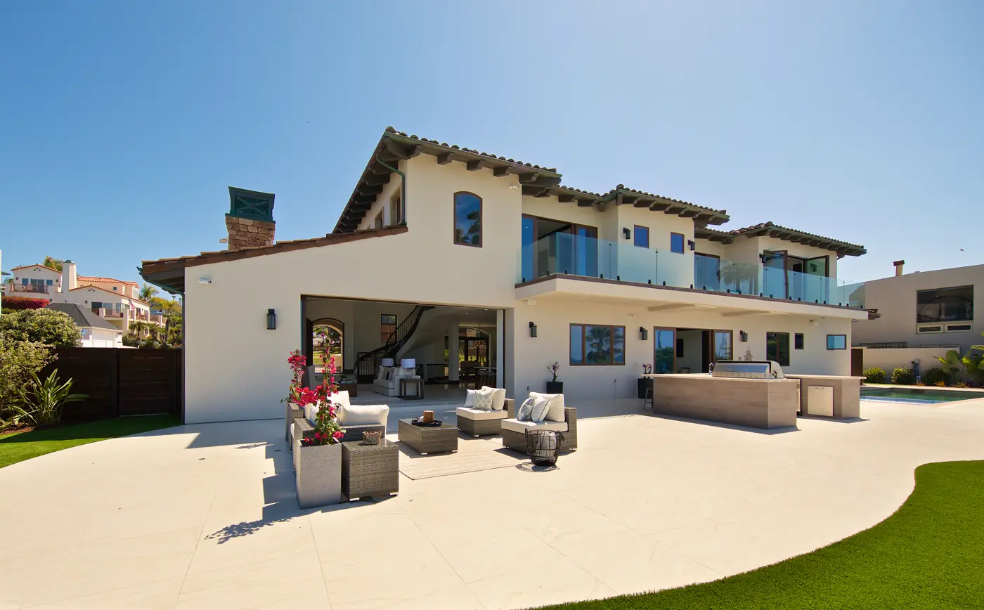 Rear elevation of a custom home with an outdoor kitchen, built-in grill, pool, and upper-level glass balcony