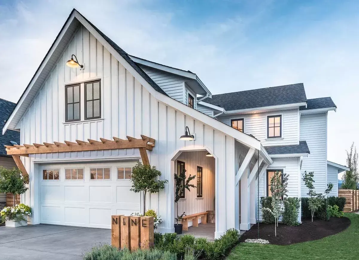 Modern farmhouse custom home with board-and-batten siding, timber pergola, and stone landscaping at dusk
