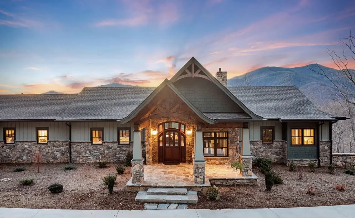 Custom mountain-style home with timber entry, stone base, and gabled roofline at sunset