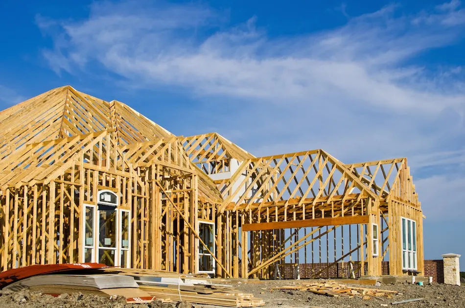 New building under construction with roof trusses and framed walls against a blue sky
