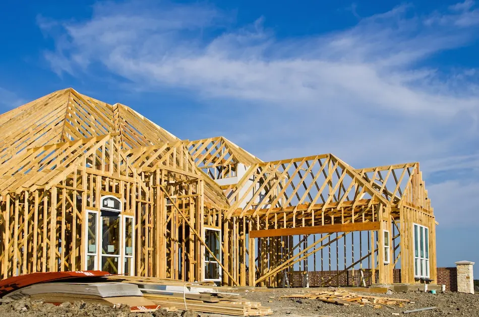 Building under construction with roof trusses and framed walls against a blue sky